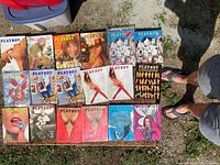 Photo showing 20 vintage Playboy magazines arranged on a wooden surface outdoors with various covers visible