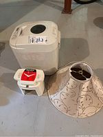 All three items: Breadman bread maker, Veg-O-Matic food cutter, and beige lampshade on floor.