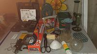 View of tools and gardening items on a table including cordless drill case, hand spreader, clamps, feeders, and gloves