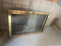 Brass fireplace insert showing the full front face with steel mesh and glass sliding doors, placed against a concrete wall.
