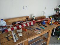 Overall overview of tools laid out on wooden workbench in garage with American flag and yard stakes on top