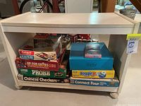 White wooden rolling cart containing stacked vintage board games showing colorful and worn boxes.