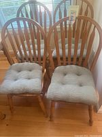 Four wooden kitchen chairs arranged together with cushioned seats in front of a window with blinds. Shows overall lot contents and condition.
