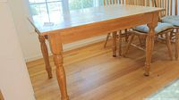 Photo showing the front and side view of the solid wood kitchen table with turned legs and part of a cushioned wooden chair.