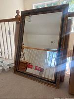 Full view of the vintage wall mirror showing gold and black decorative trim around the edges, reflecting a stair railing and window in the background.