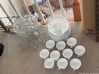 Wide shot showing pressed glass punch bowl with intricate starburst and geometric patterns, 7 matching glasses, and milk glass set with cups and plates stacked.