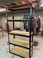 Full view of one metal rack shelf unit with 4 beige pressed board shelves against basement background.