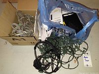 Box of bundled cables, blue plastic bag containing Netgear router box, tangled Christmas lights, black headphones on top
