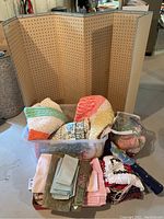 Full view of foldable pegboard sewing panel with assorted textiles and craft items in front including crochet blankets, towels, napkins, placemats, Christmas potholders, mailbox cover, and skeins of wool.