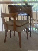 Front view of the sewing chair and table showing upper part of chair's cushioned seat and one drawer of sewing table