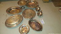 Photo of silver plated serveware assortment including platters, compotes, cream pitcher, and sugar bowl marked Reed & Barton, Poole EPCA Bristol silver, W. M. Rogers, and unmarked pieces on a table.