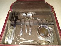 Silver plated flatware set displayed in a velvet-lined case showing knives, forks, spoons, butter knives, sugar tongs, and coasters.