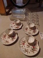 Photo showing two sets of floral tea cups and matching saucers, along with clear glass cups and rectangular glass trays placed on a basement floor.