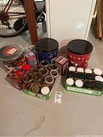 Wide view showing all tin containers and glass jars arranged on basement floor with bicycle visible in background