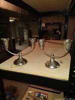 Pair of Raimond Sterling weighted silver candle holders placed on a shelf in a basement setting shown from a front angle.