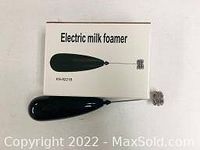 Top view of the electric milk frother laid on its box, showing black handle and stainless steel whisk head.