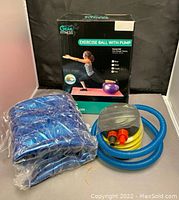Blue exercise ball sealed in plastic with yellow accordion foot pump and blue hose with nozzles, box in the background.