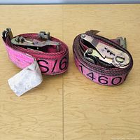 Two rolled pink ratchet straps side by side on a wooden surface showing metal ratchet mechanisms.
