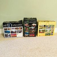 Photo showing three boxed sets of jigsaw puzzles: two Art Gallery 10 sets on the left and middle, and one Glorious Gardens 10 set on the right. Boxes show some wear and use.