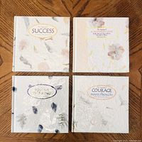 Four square-format books with handmade paper covers featuring leaves and floral inclusions. Covers show titles: Success, A Mother's Love, Positive Thinking, Courage Inner Strength.
