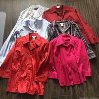 Lot of 6 blouses arranged on wooden floor: various colors and patterns including striped, solid red, and vibrant pink.
