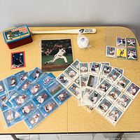 Full overview of the lot showing all items: unopened vintage baseball card tin, mini souvenir bat, mini baseball, Roger Clemens photo, and baseball cards spread out on table.
