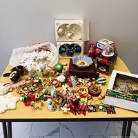 Photo of a table covered with various Christmas ornaments including glass baubles, fabric birds, small stuffed animals, stars, and snowflakes.