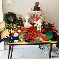 Photo showing assorted Christmas decorations on a table including wreaths, glass ornaments, figurines, candles, and a tall elf door decoration