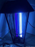 Close up image showing bug zapper illuminated with UV light tubes glowing inside metal wire cage.