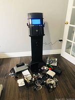 Full view of Akai karaoke machine, various electronics, power adapters and cables laid out on floor.