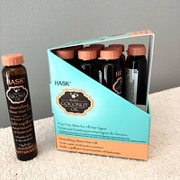 12 amber plastic vials of Hask Monoi Coconut Oil hair oil in turquoise and orange partially open display packaging, showing clear branding and product text.
