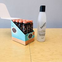 Image showing the display box with twelve Hask Nourishing Shine Hair Oil vials and the Ramoni Silk Oil bottle side by side.