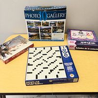 Top view of several jigsaw puzzle boxes on a yellow table, showing Photo Gallery 10, crossword puzzle, wildlife and Springbok puzzles.