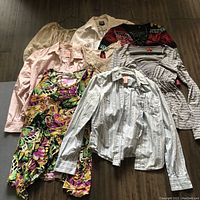 Eight ladies tops laid out flat, showing variety of styles and colors including patterned, striped and solid colors.