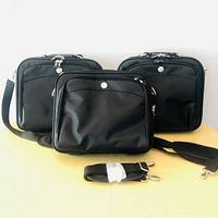Three black Dell laptop bags shown standing upright on a light wooden surface. Two bags with shoulder straps attached, one strap detached and placed in front. Each bag has a simple smooth black exterior with silver zippers and buttons.