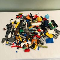 Front view of a pile of assorted loose LEGO pieces of various shapes, sizes, and colors spread on a white surface.