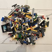 Assorted loose Lego pieces spread out on the floor, showing variety of colors, shapes, and some architectural elements like ladders and windows.