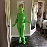 Full view of a person wearing the chromakey green spandex onesie suit indoors, showing fit and coverage of suit including feet and head.