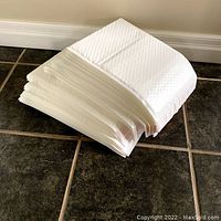 Stack of new white vinyl padded mailer envelopes on floor showing thickness and stacked quantity