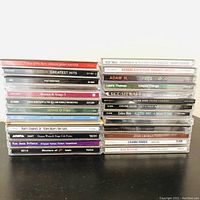Full stack of 27 assorted music CDs, with visible artist names and album titles, standing upright on a shelf.