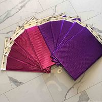 Ten large metallic bubble mailers laid out in a fan arrangement on a floor, 5 pink and 5 purple.