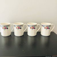 Set of four white fine china coffee mugs with autumn fruit design in a row, showing the consistent pattern on each mug.