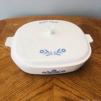 Front and top view of the white ceramic casserole dish with blue cornflower pattern and lid on wooden table.
