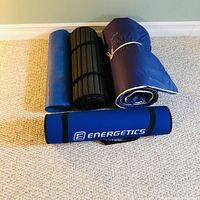 Four yoga mats, rolled and folded, showing brand Energetics on blue mat and a black ribbed mat, two older mats in various conditions.