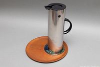 Full view of the stainless steel carafe on the teak and glass serving tray against white background.
