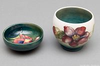 Two Moorcroft porcelain pieces side by side on a grey background showing floral designs and interior glazing.