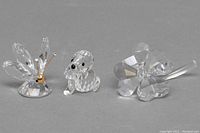 Front view of three Swarovski crystal figurines: butterfly, puppy with damage, and 4-leaf clover.