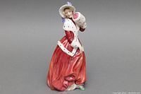 Front view of 7.5-inch Royal Doulton porcelain figurine in red dress holding muff with white fur trim and purple floral hat.