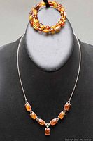 Front view of necklace displayed on black stand with wrapped beaded amber bracelet above it.
