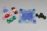 Set includes a blue fused glass square ashtray, assorted blown glass candies, and glass olives arranged on a surface.